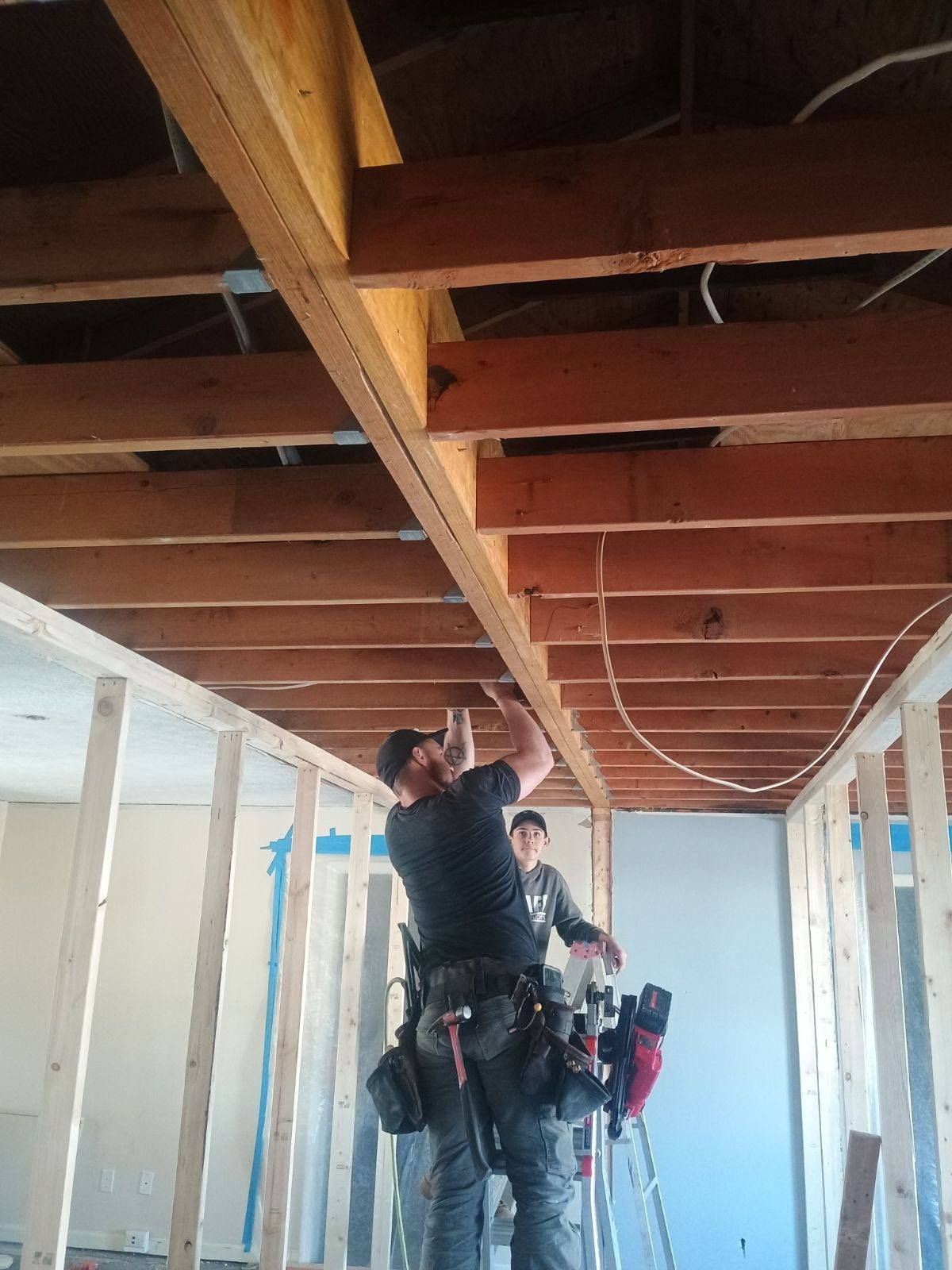 Workers installing wiring in a ceiling crawlspace with exposed wooden beams and white wall framing