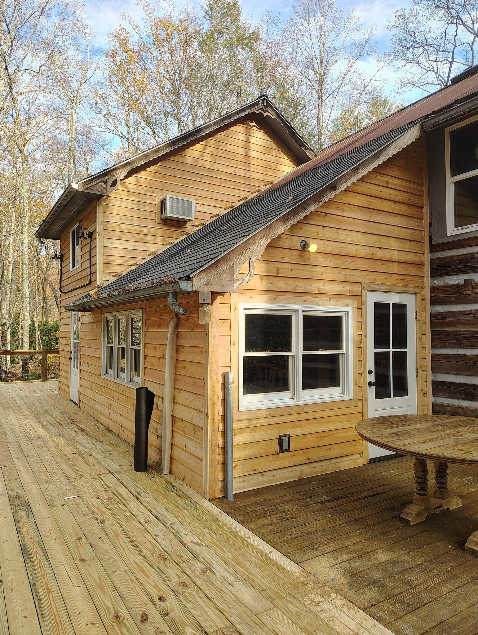 Wooden cabin with dark roof and deck, set among trees in a forested setting.