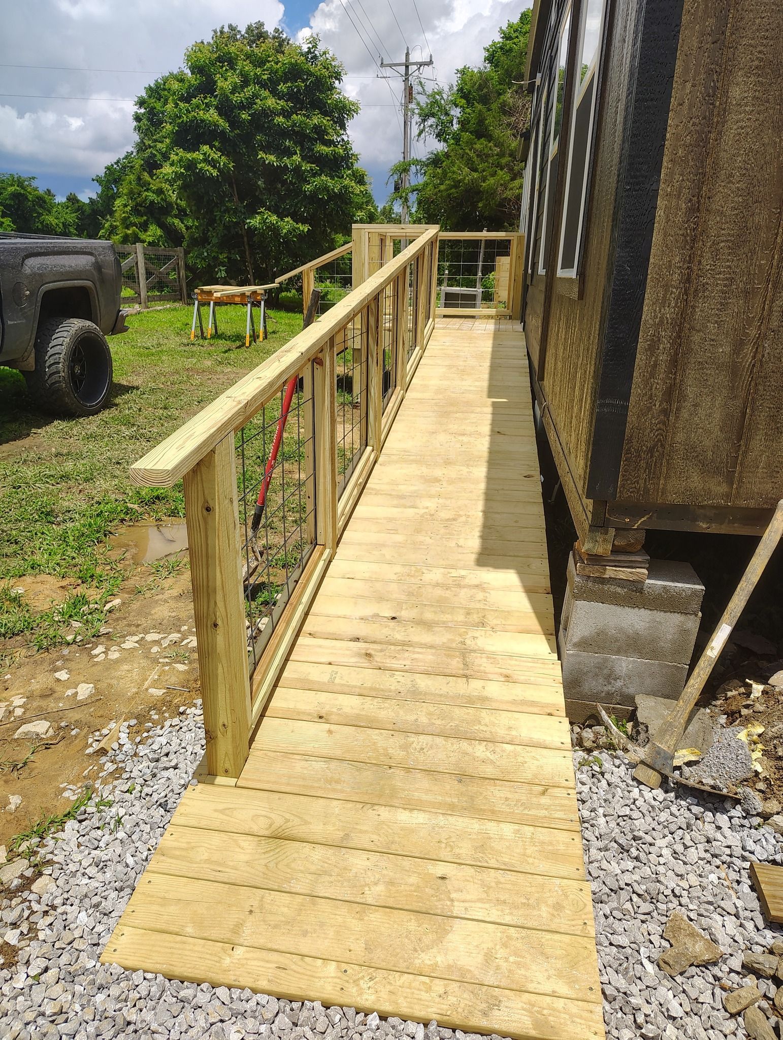 Wooden wheelchair ramp with handrails beside a building, leading over gravel to a grassy outdoor area.