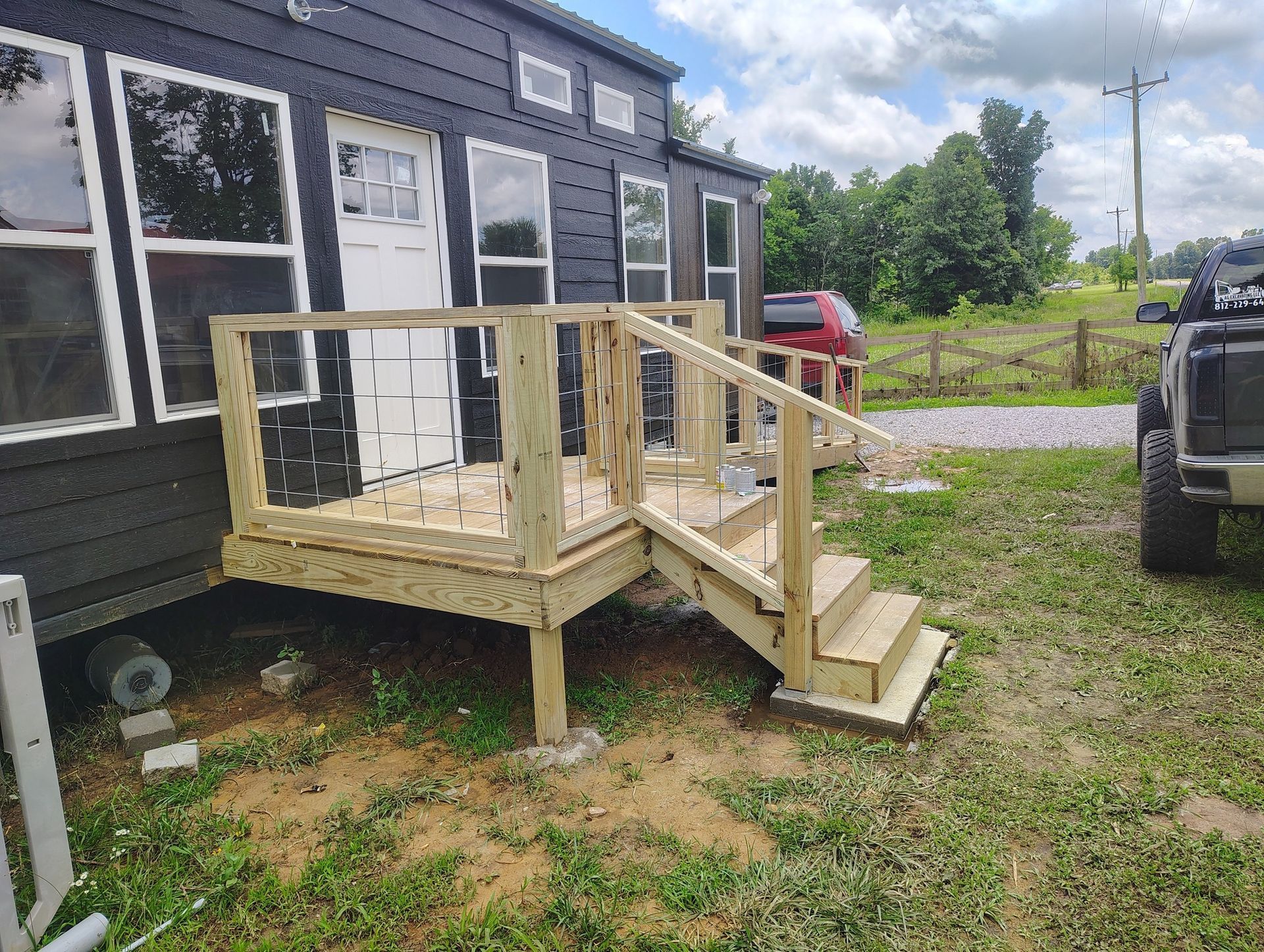 Small wooden porch and stairs attached to a dark building in a grassy yard.