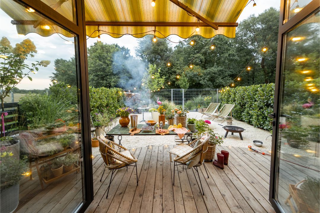 A white house with a dark roof and a retractable striped awning covering a wooden patio with an outdoor dining set.