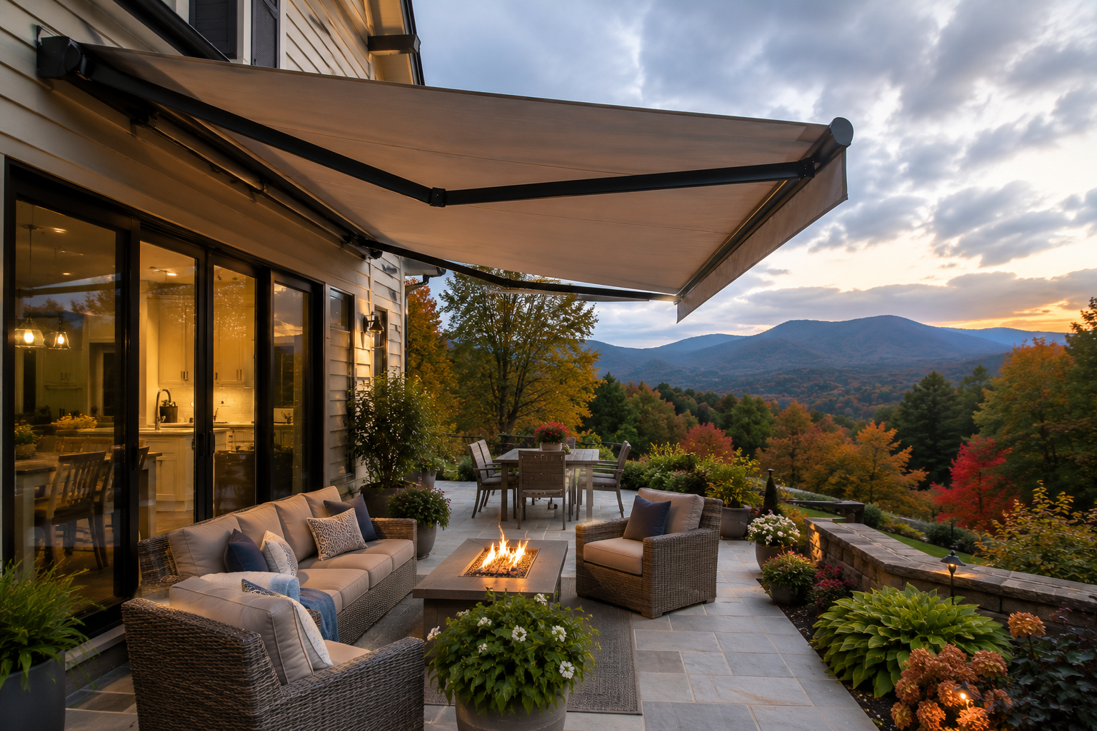 Cozy patio with cushioned seating, fire pit, motorized awning, and mountain sunset view beside a glass-walled home