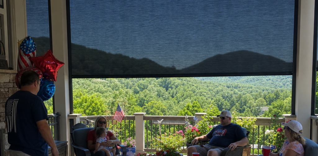 Porch view, shaded by patio shades, of people relaxing under red balloons, overlooking a sunlit green valley and distant mountains