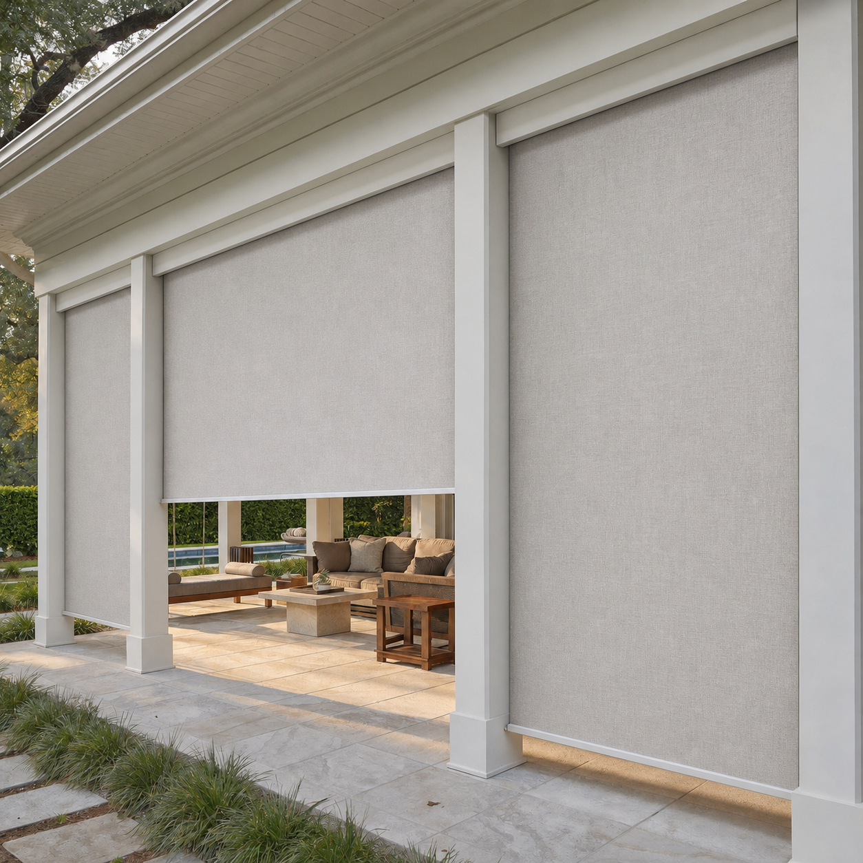 Three gray outdoor motorized patio shades cover a patio opening in front of a house