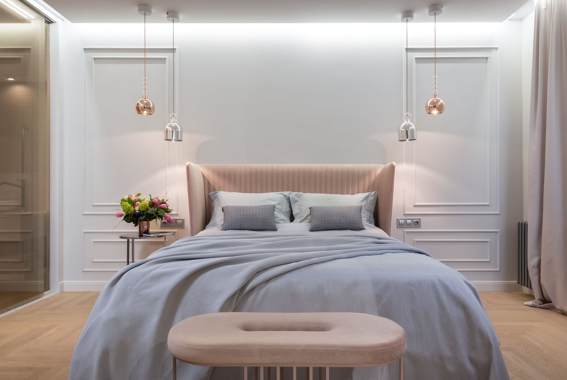 Bedroom with light wood floor, upholstered headboard, two pendant lights, and decorative wall molding.