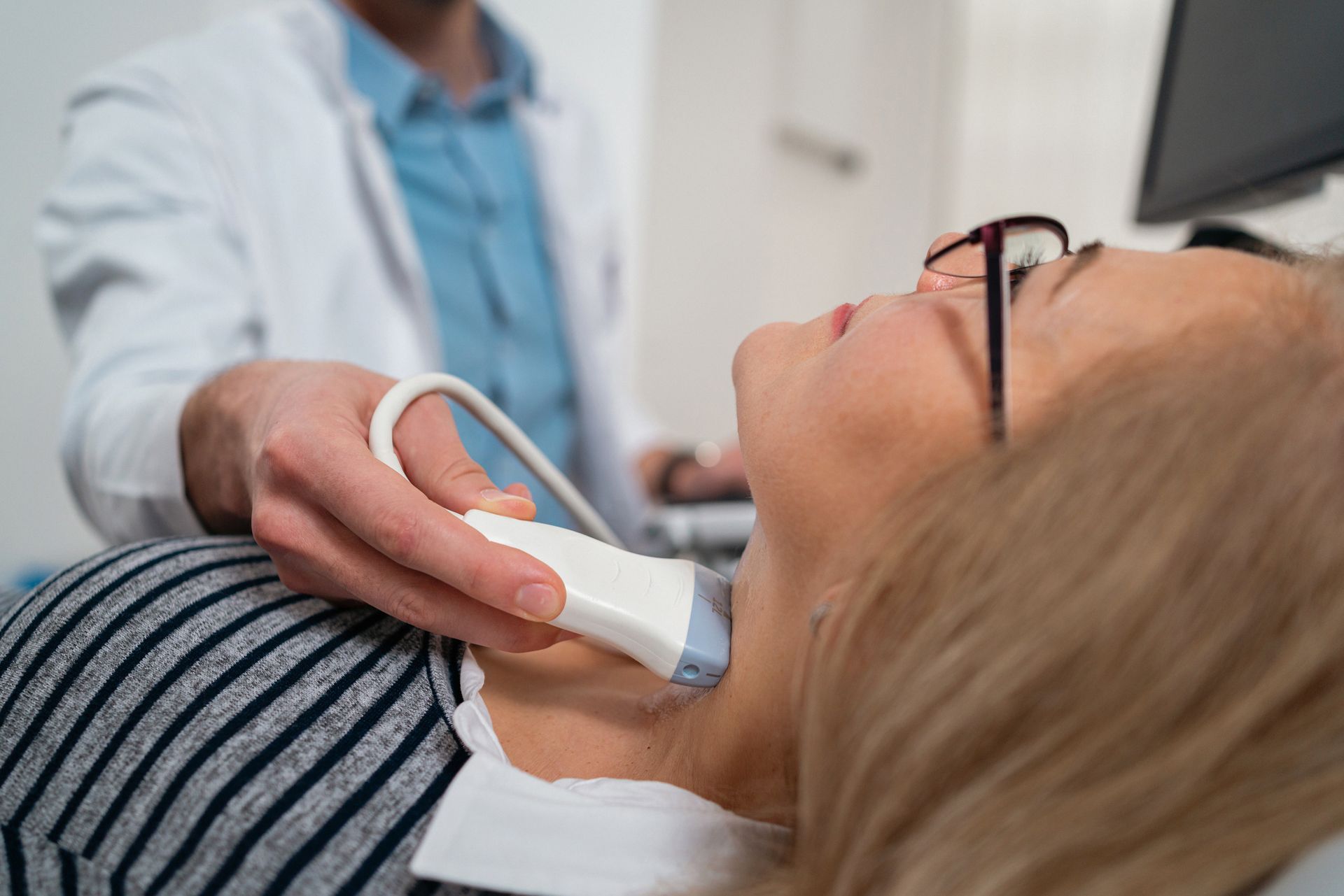 Donna sottoposta a ecografia del collo. Il medico tiene la sonda sul collo in ambiente medico.