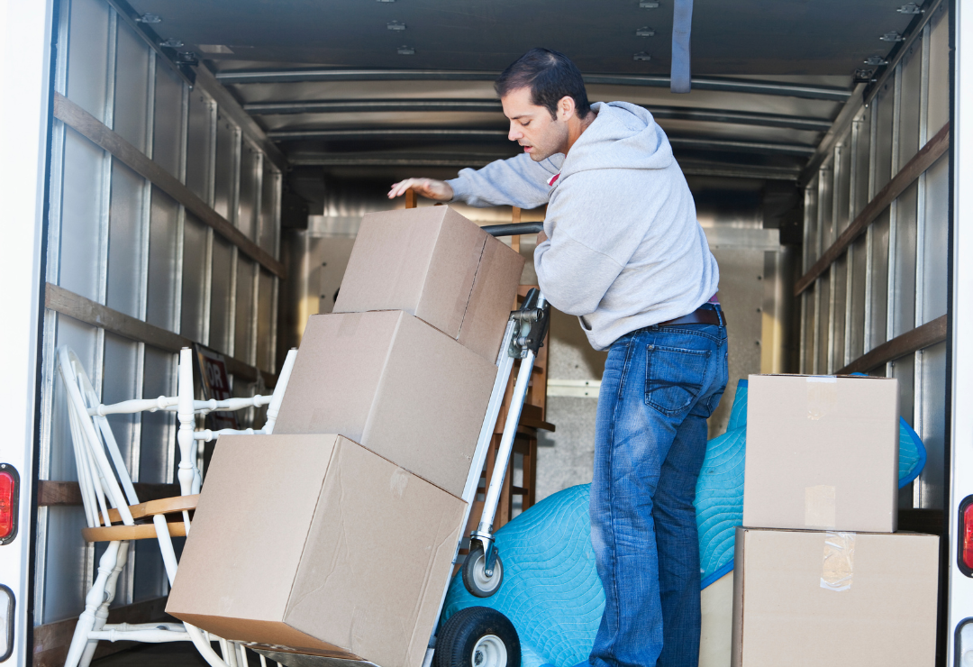A man with a dolly moving cardboard boxes inside of a box truck