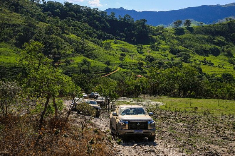 Veículos todo-terreno percorrem um caminho lamacento através de uma paisagem verdejante e montanhosa.