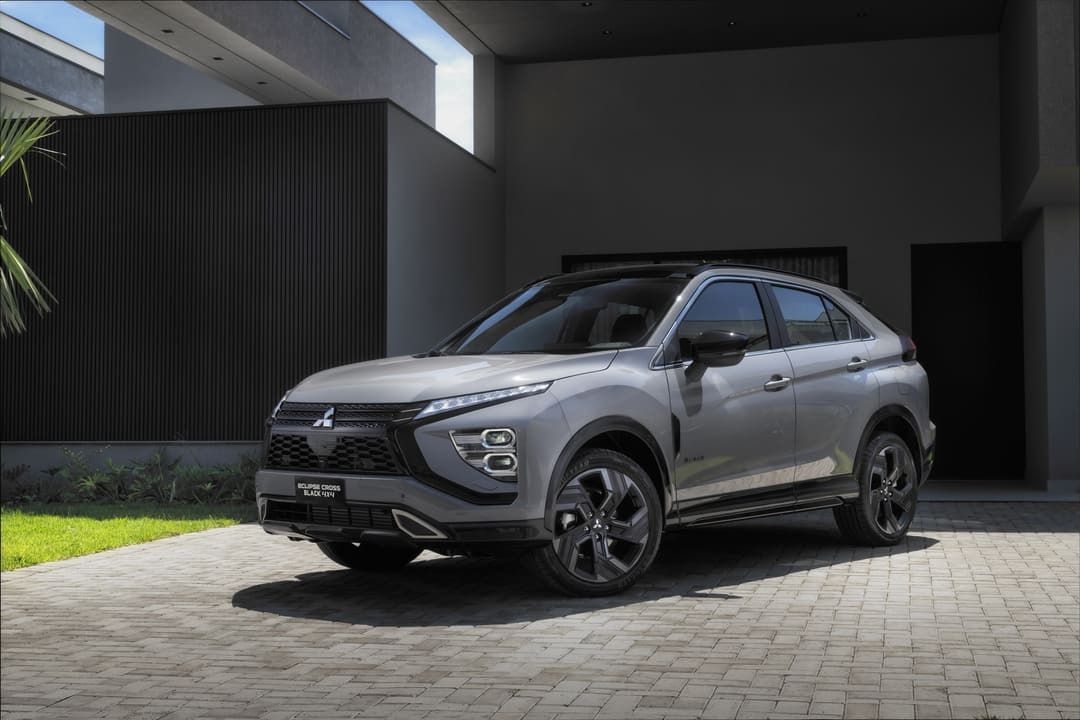SUV cinza estacionado em frente a um prédio moderno preto, em uma entrada pavimentada e ensolarada.