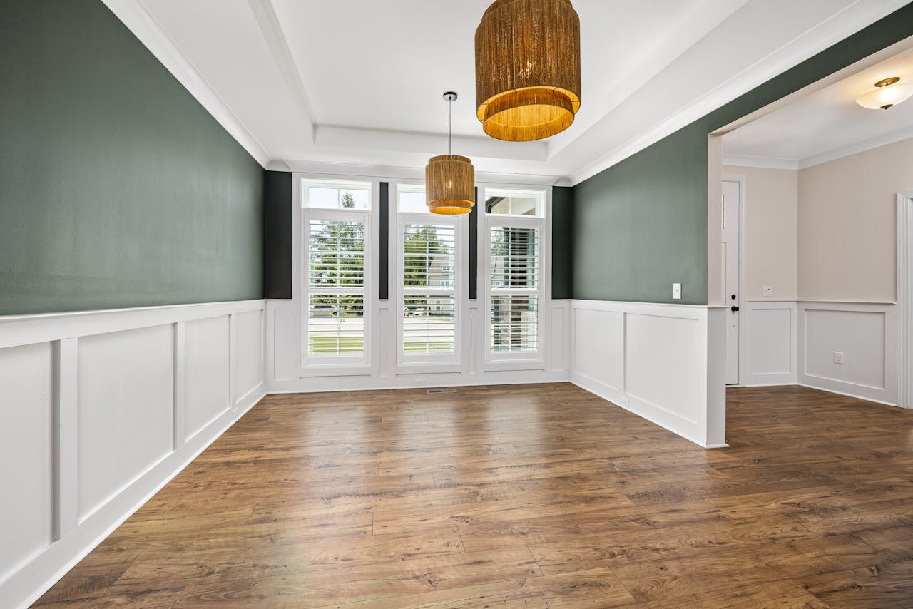 An empty dining room with hardwood floors and green walls.
