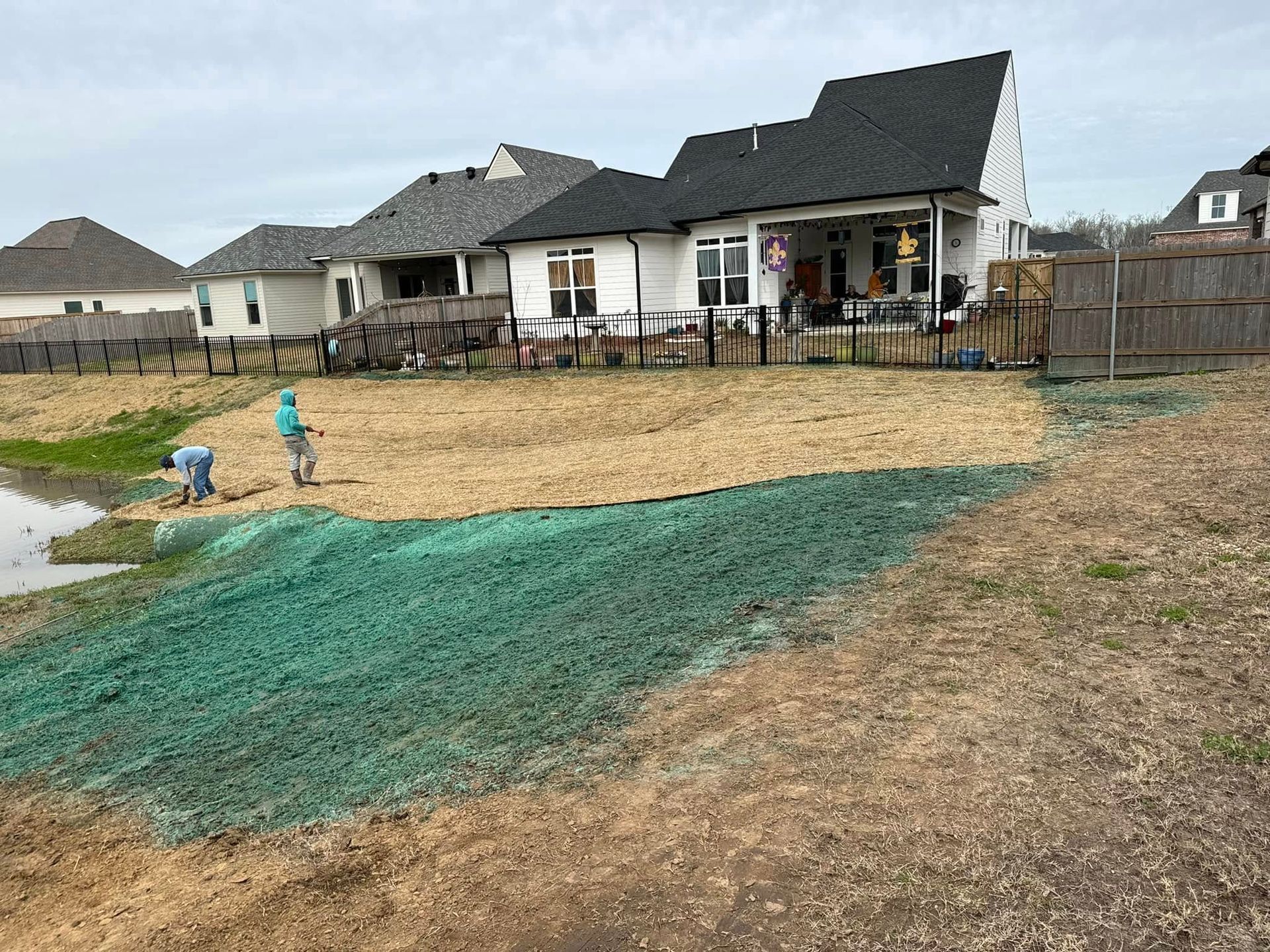 Flooded backyard beside a white house under construction, with green erosion blanket and standing water.