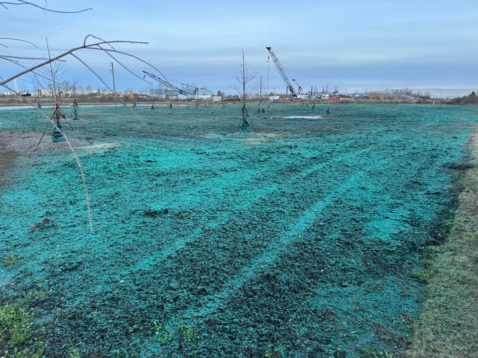 Irrigated turquoise crop field with sprinklers and farm equipment under a cloudy sky