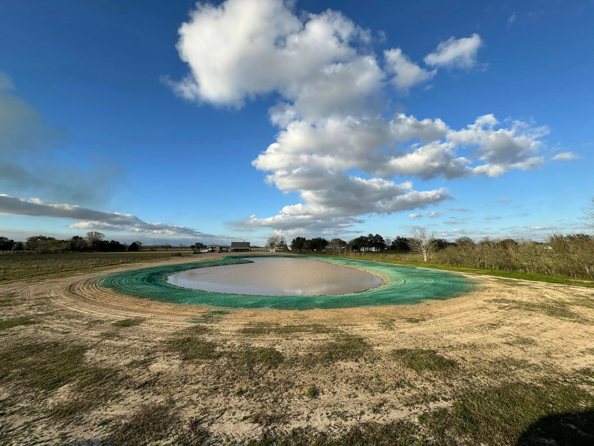 Outdoor landscape with a shallow circular pond under a bright blue sky and clouds