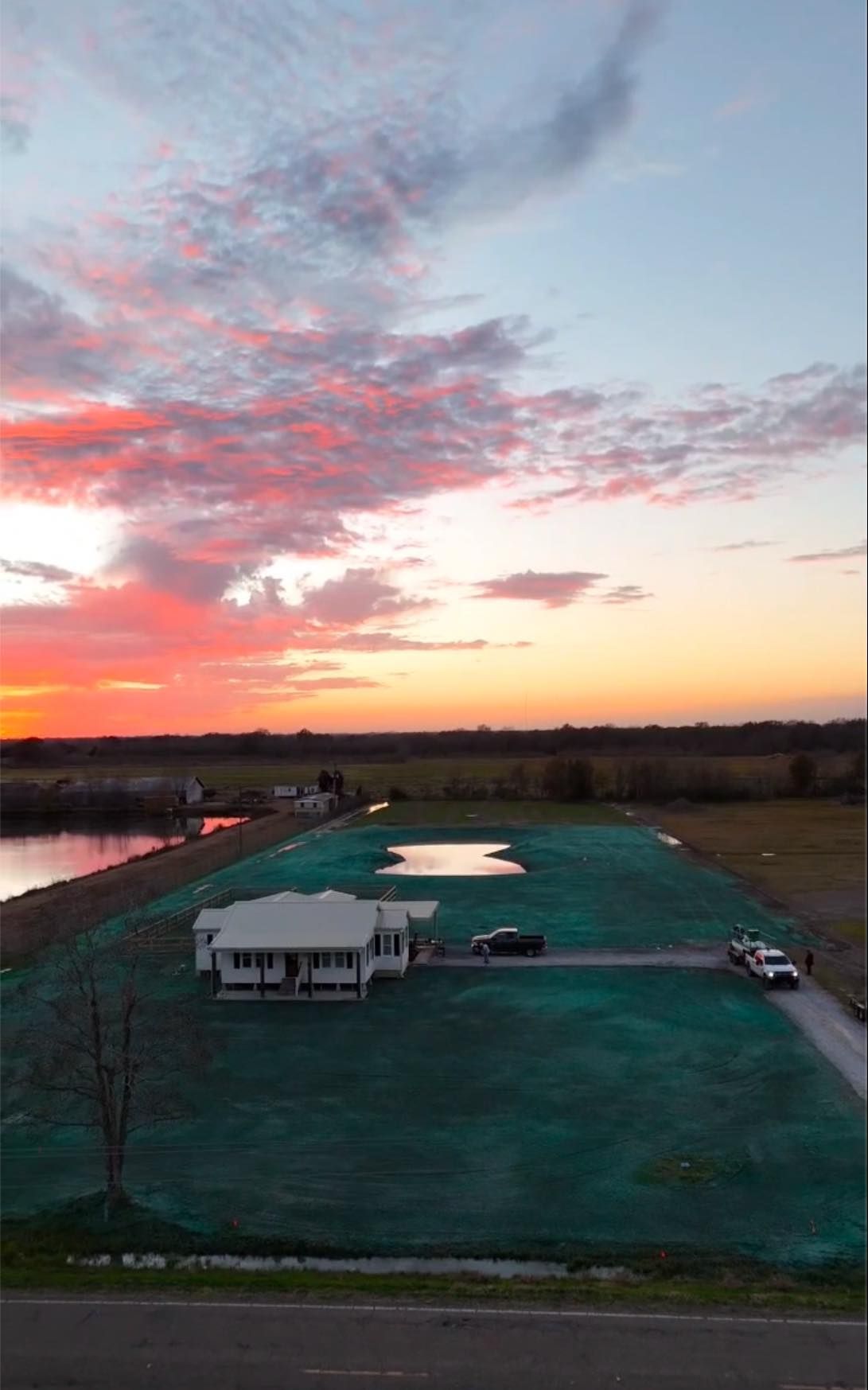Sunset over a grassy field with a white pavilion, parked vehicle, and a pink-clouded sky