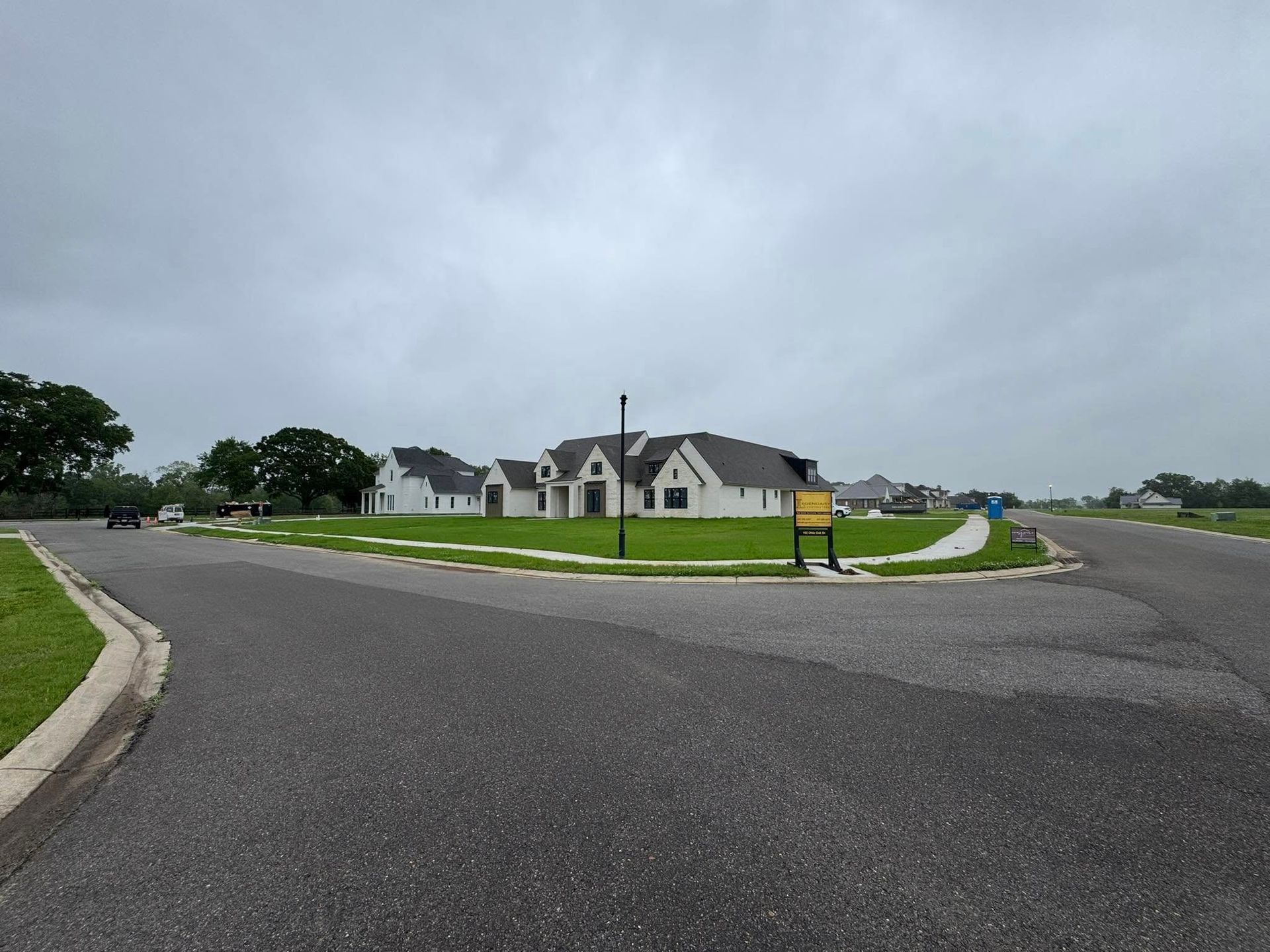 Wide suburban street and roundabout with a white building under a cloudy sky