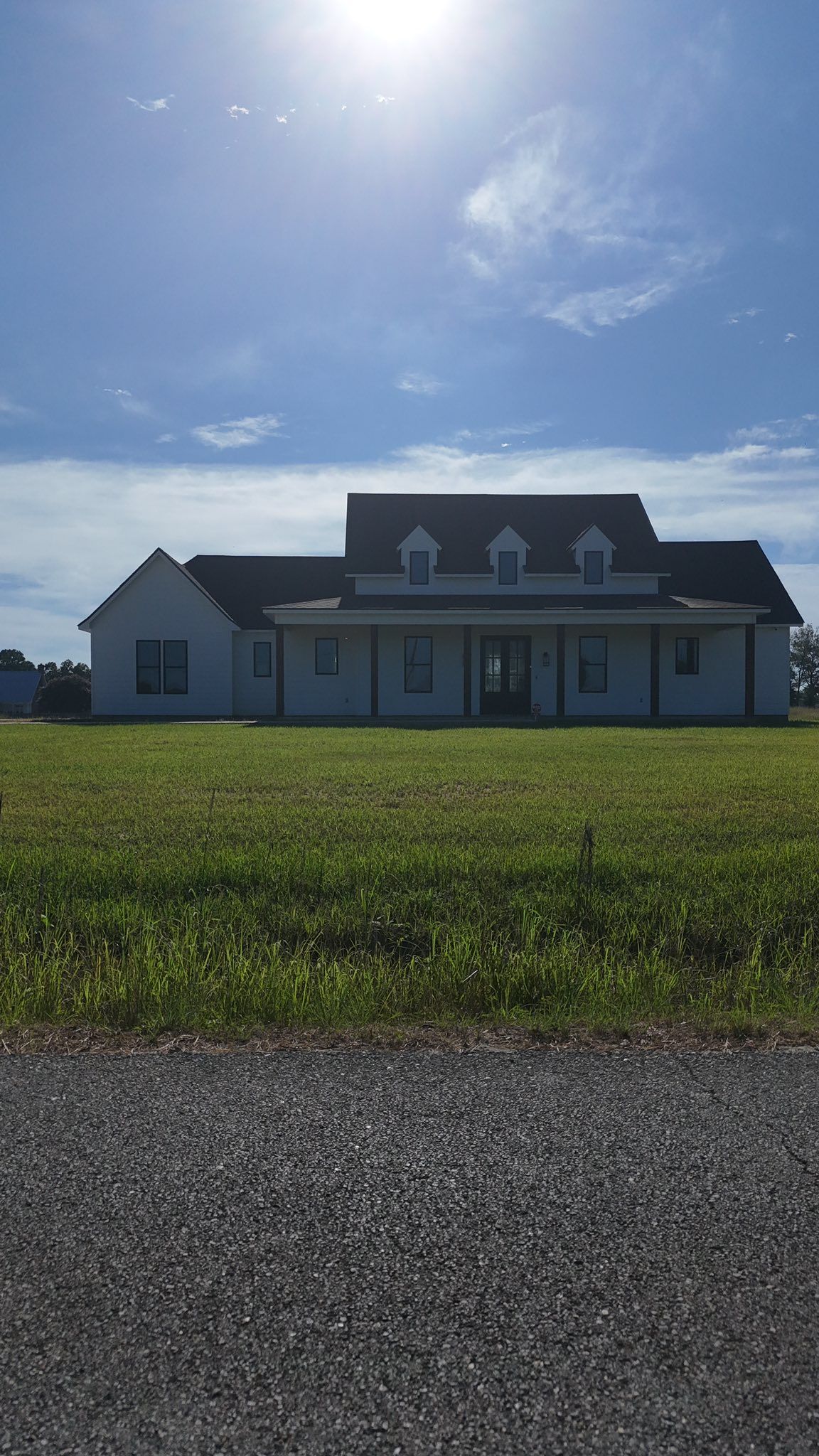 Modern farmhouse with gray roof and white siding under a bright blue sky beside a grassy field