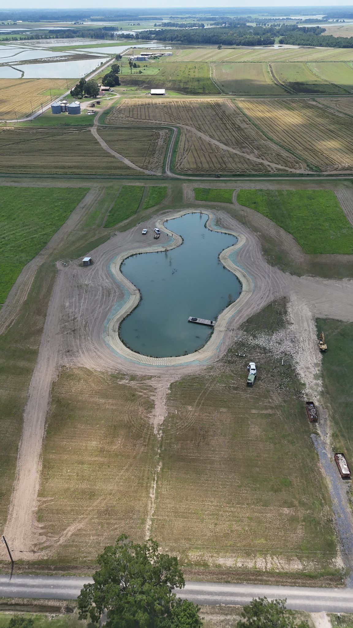 Aerial view of a landscaped pond in a grassy field with roads and open land nearby