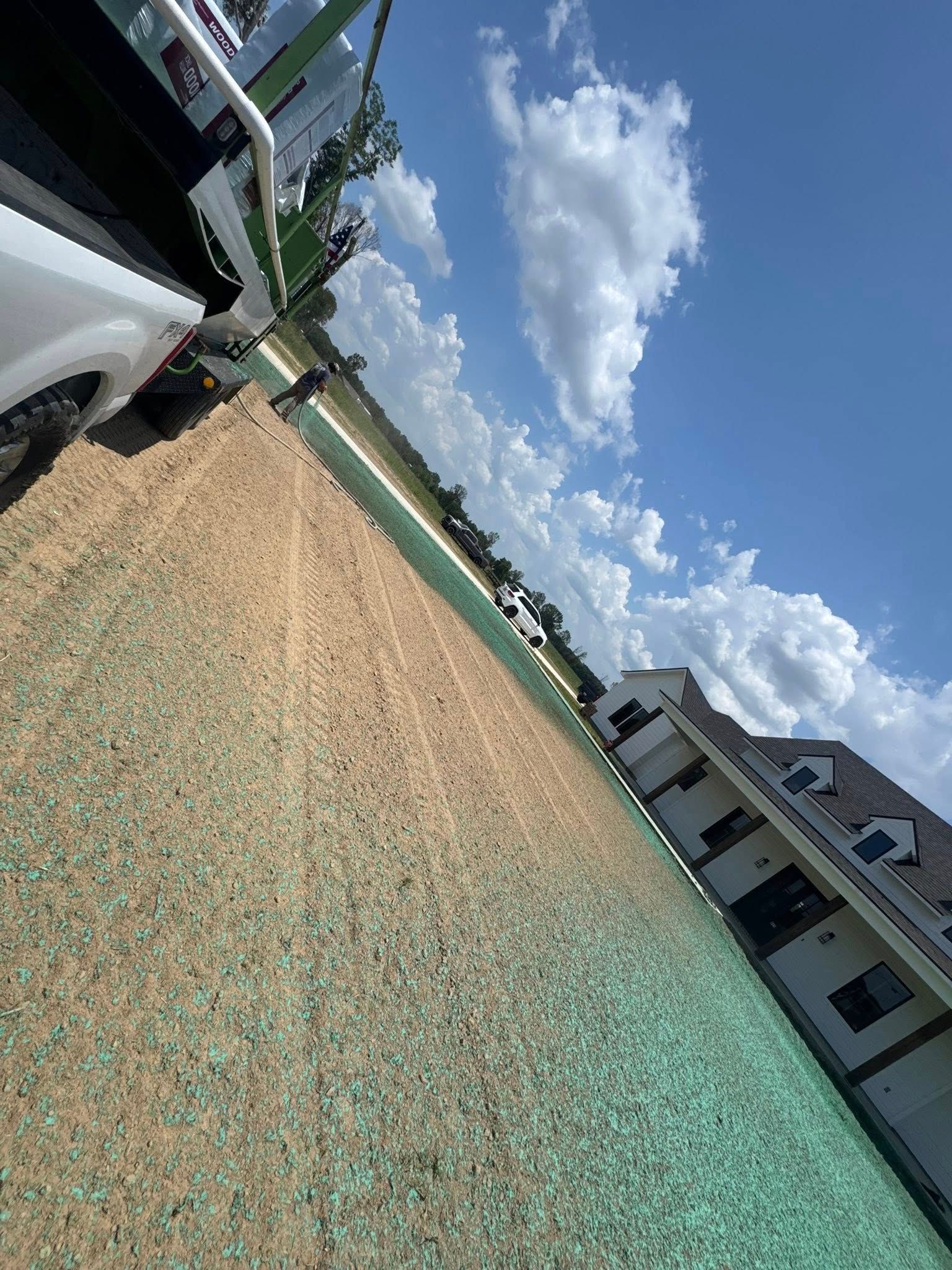 Tilted view of a gravel lot beside parked cars and a building under a bright blue sky with clouds