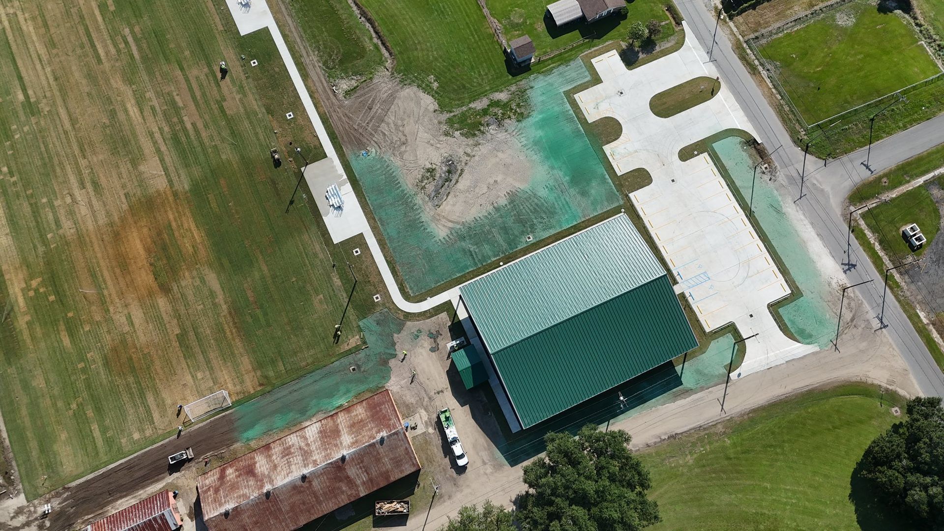 Aerial view of a farm building with a green roof beside paved driveways and grassy fields