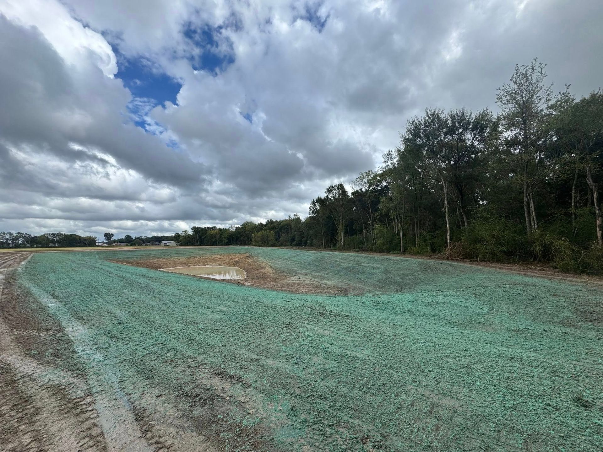 Cloudy sky over a gravel road curving through a rural, tree-lined landscape