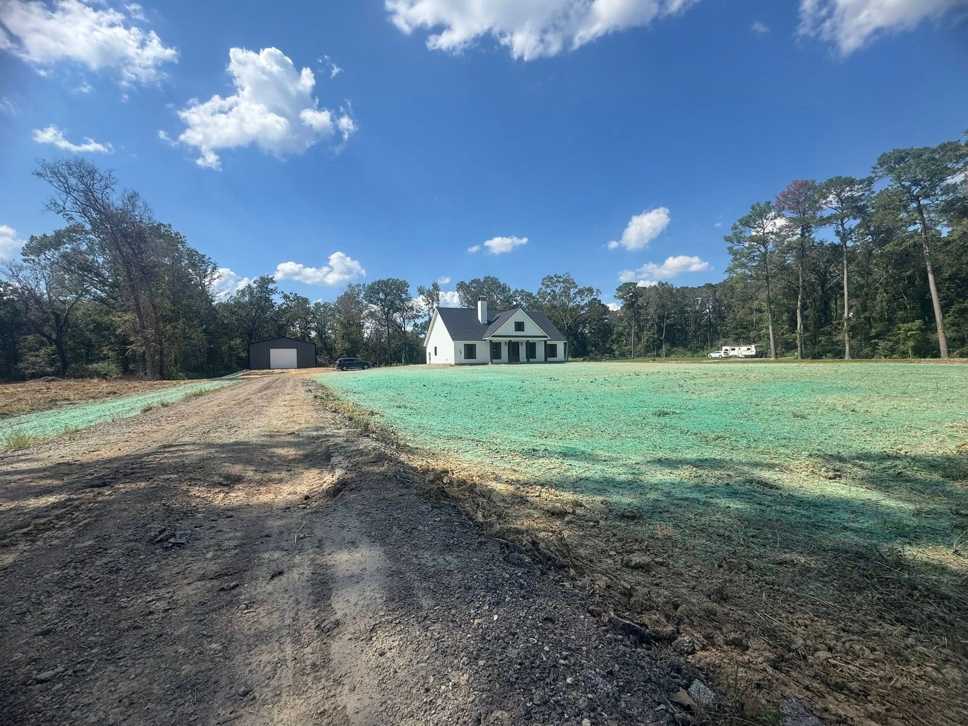 Gravel driveway leading to a white house in a grassy field under a blue sky with clouds