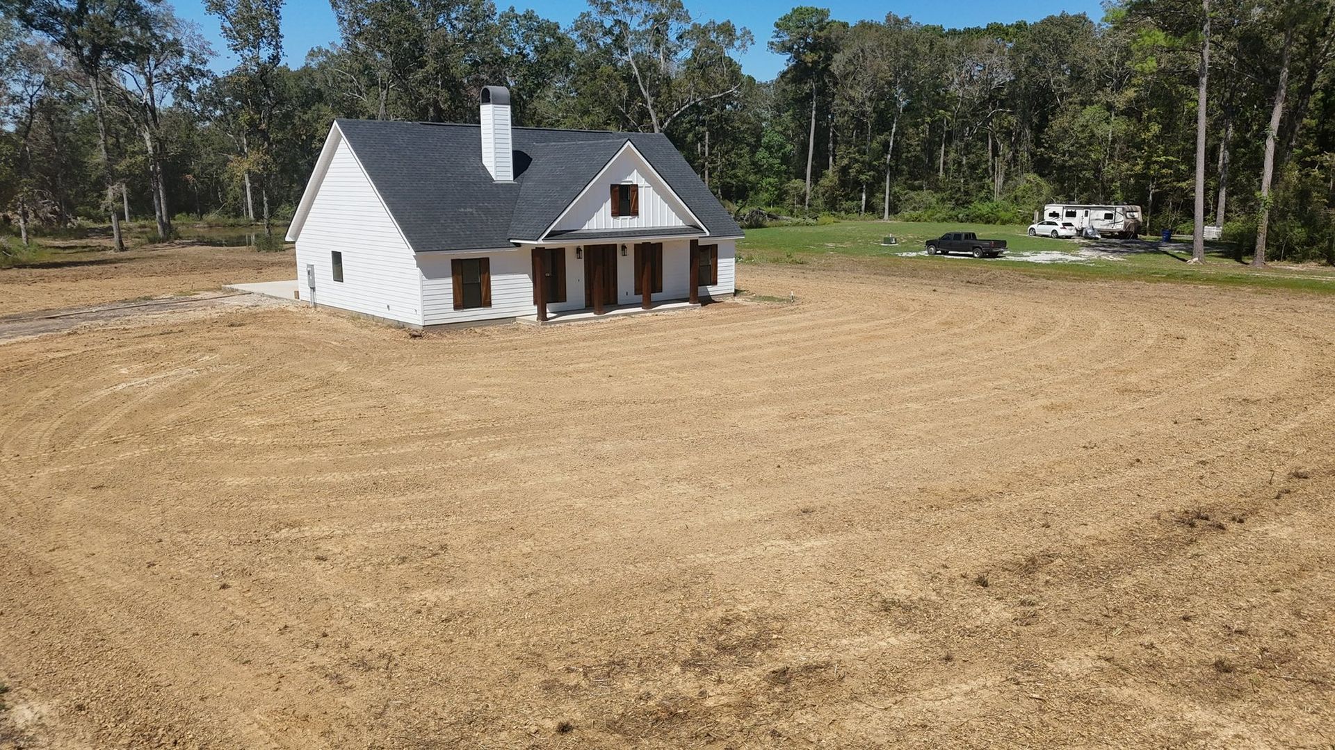 Small white house with a front porch in a dry, open field bordered by trees