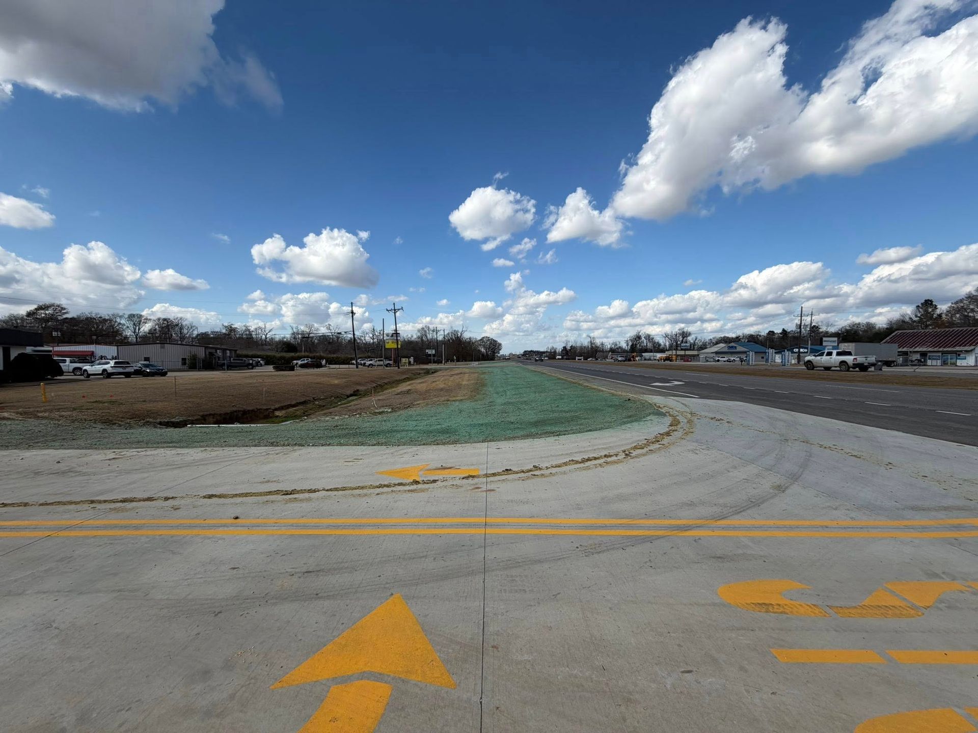 Empty airport taxiway under a bright blue sky with clouds, marked by yellow arrows.