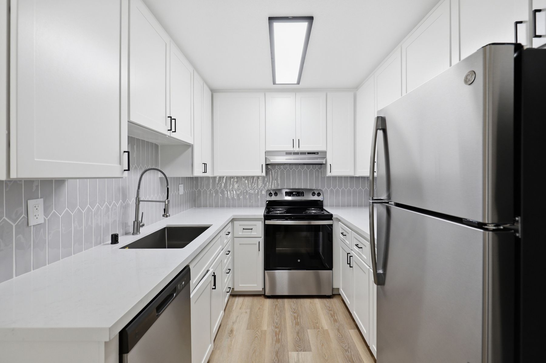 Bright modern galley kitchen with white cabinets, stainless appliances, and light wood floor
