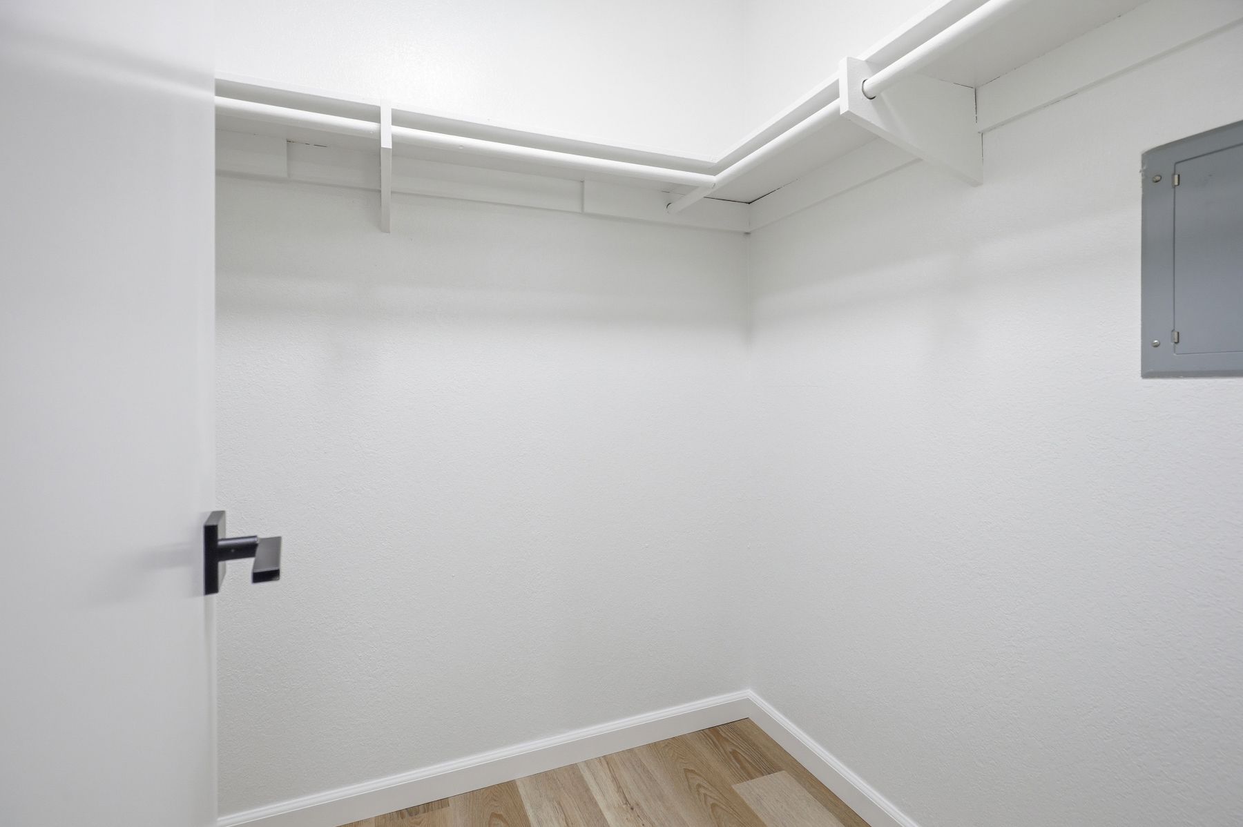 Empty white walk-in closet with hanging rods and wood flooring