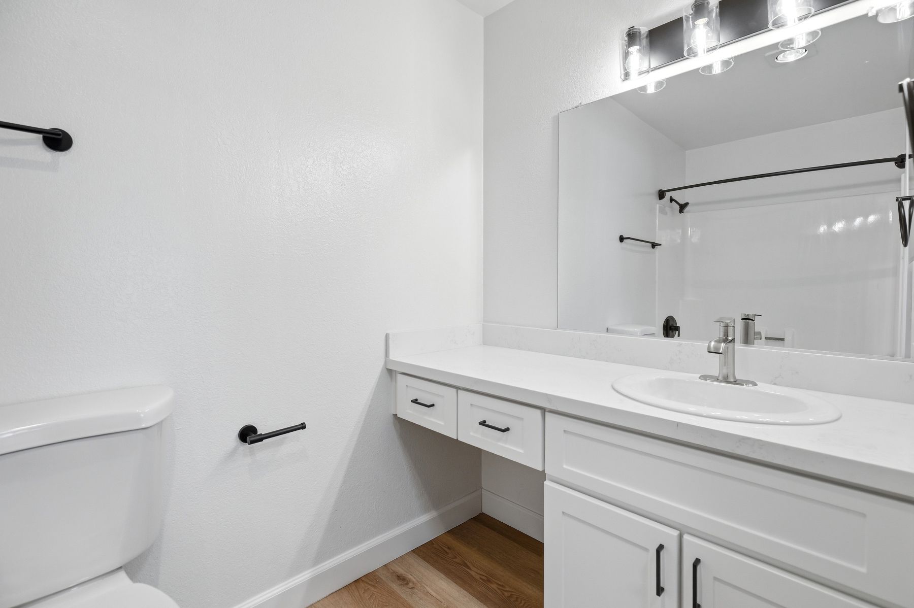 Bright white bathroom with long vanity, mirror, and toilet partially visible on the left.