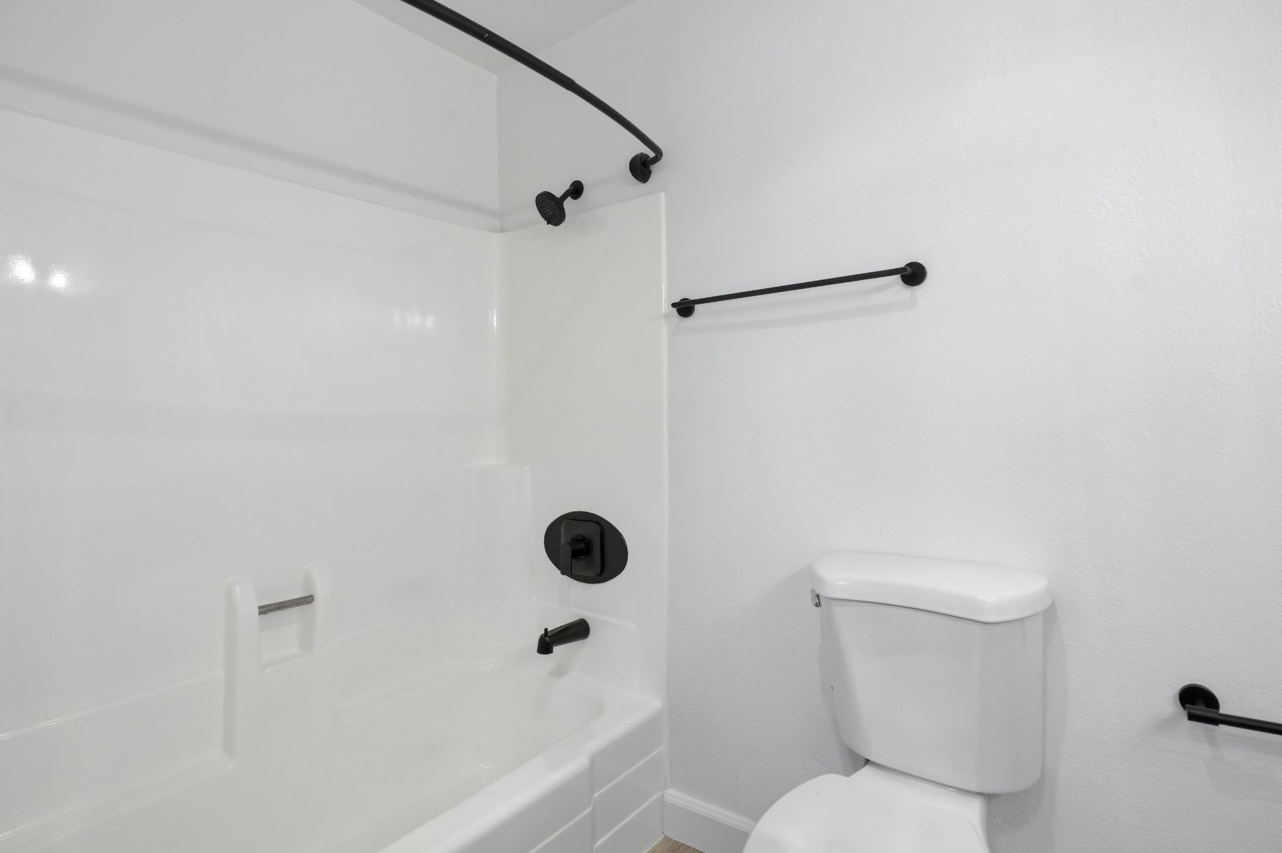 Bright white bathroom with bathtub, toilet, black shower fixtures, and grab bars