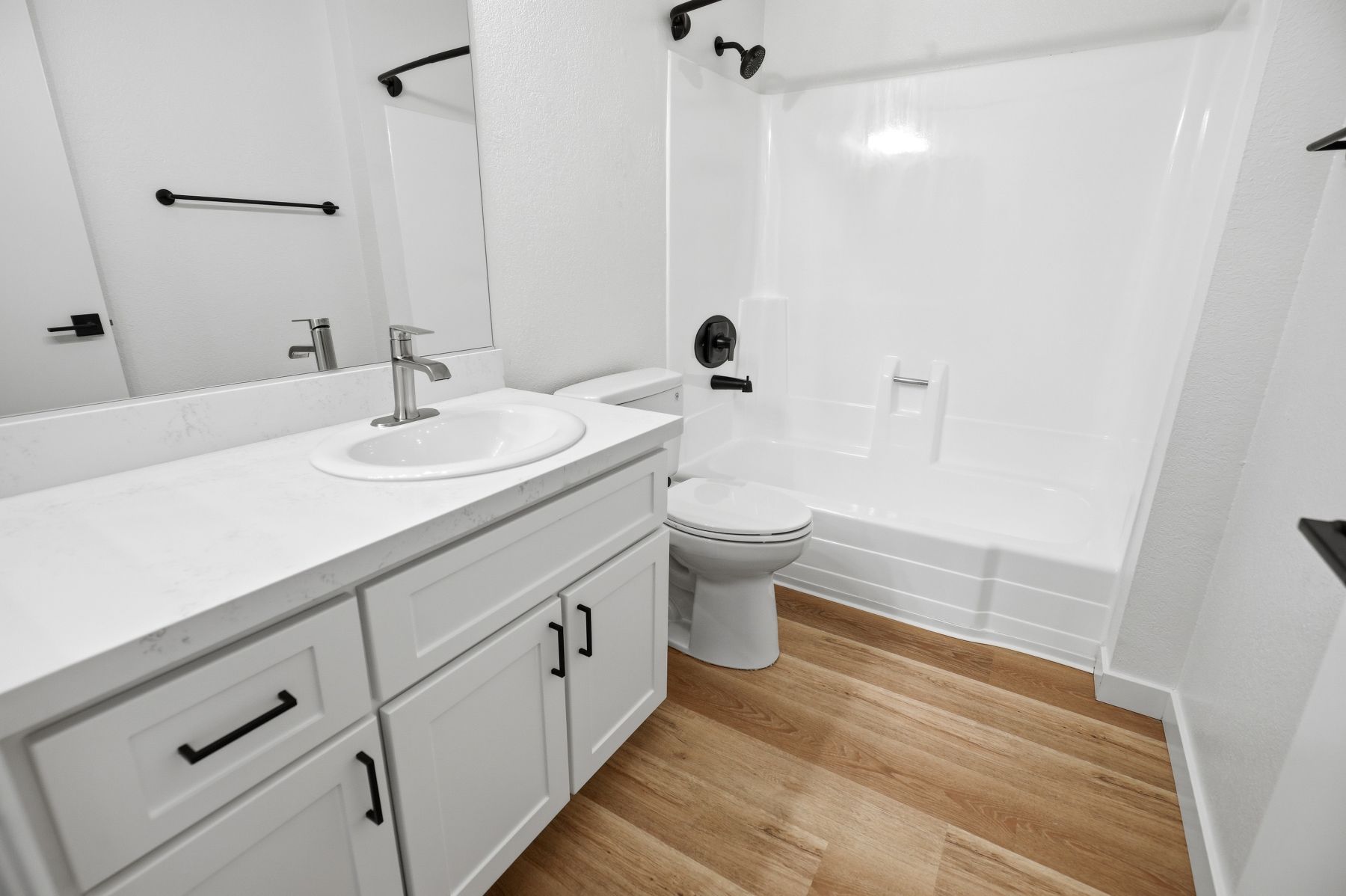 Bright white bathroom with vanity, sink, toilet, and wood-look floor.