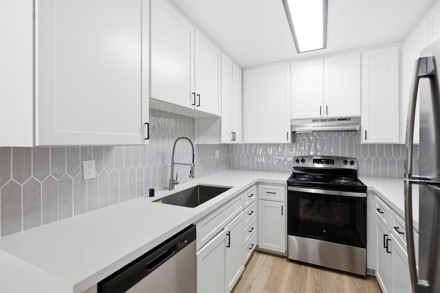 Bright modern galley kitchen with white cabinets, gray tile backsplash, stainless appliances, and wood floor
