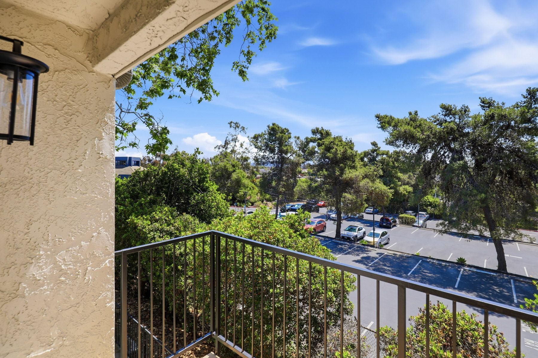 Balcony view of a tree-lined street with parked cars and blue sky