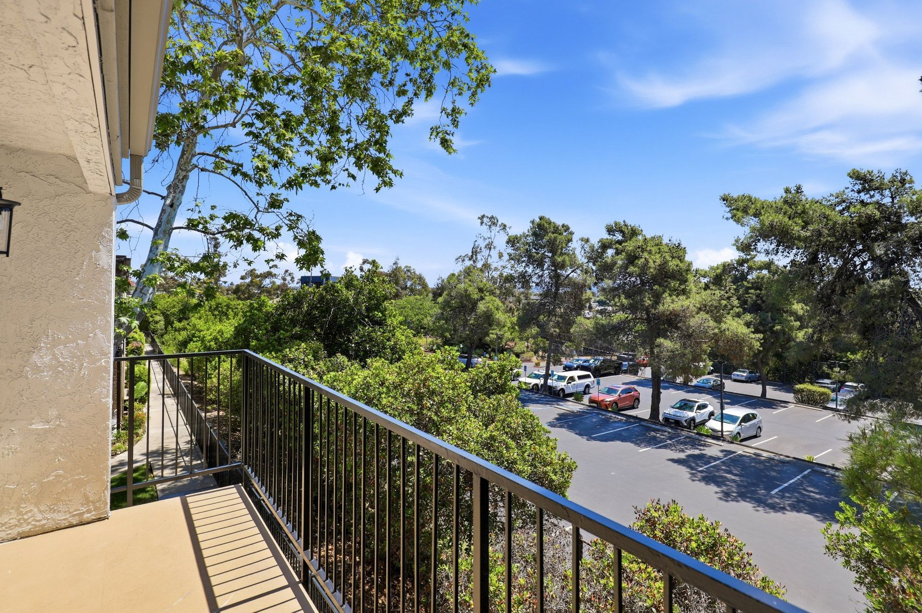 Balcony overlooking a sunny parking lot and trees under a blue sky