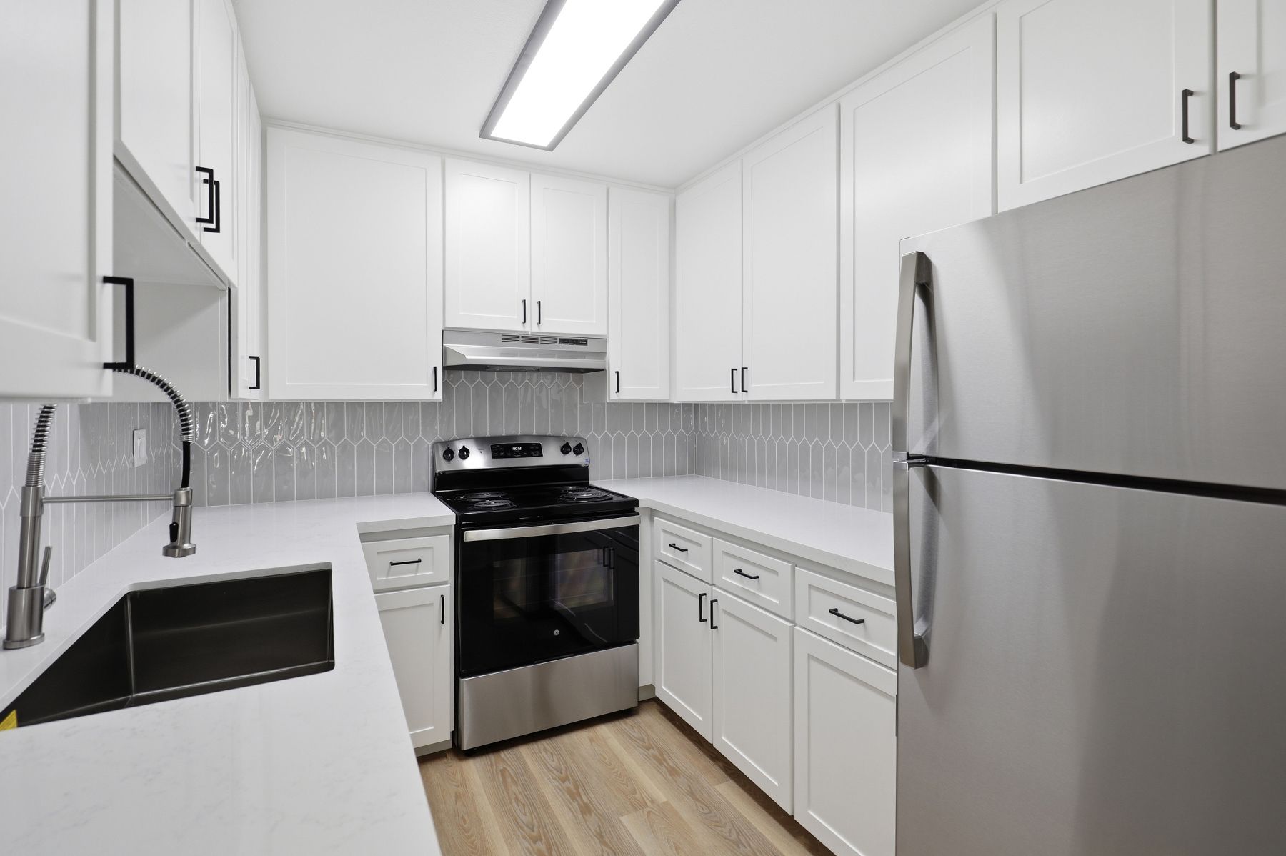 Bright white modern kitchen with stainless steel appliances and black countertops.