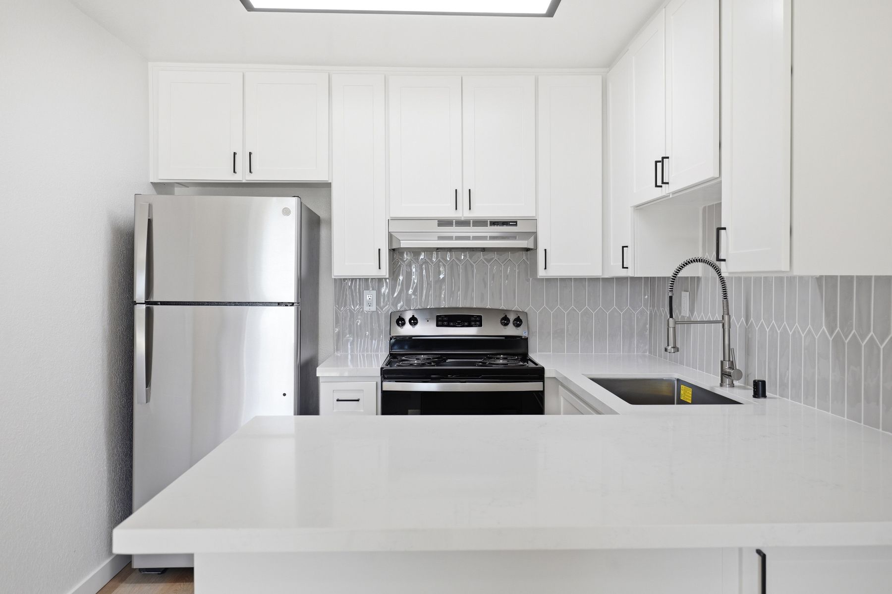 Modern white kitchen with stainless steel appliances, white cabinets, and a large island counter