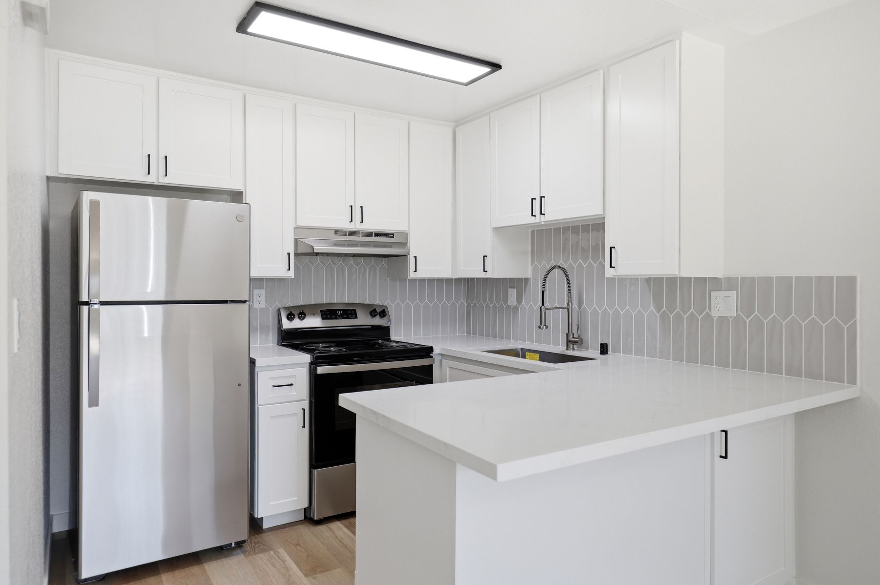 Bright white kitchen with stainless steel appliances and a peninsula counter.