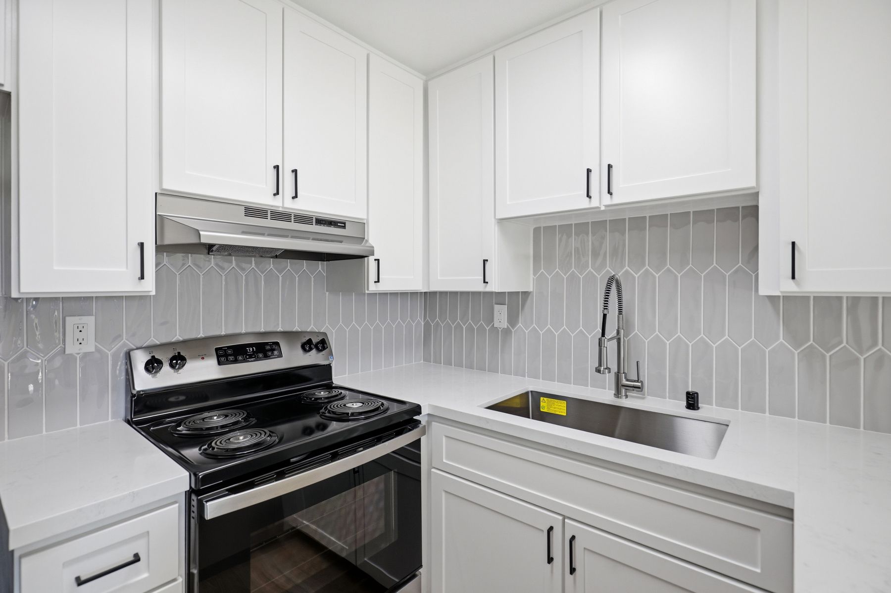 Modern white kitchen with stainless steel stove, sink, and hexagon tile backsplash
