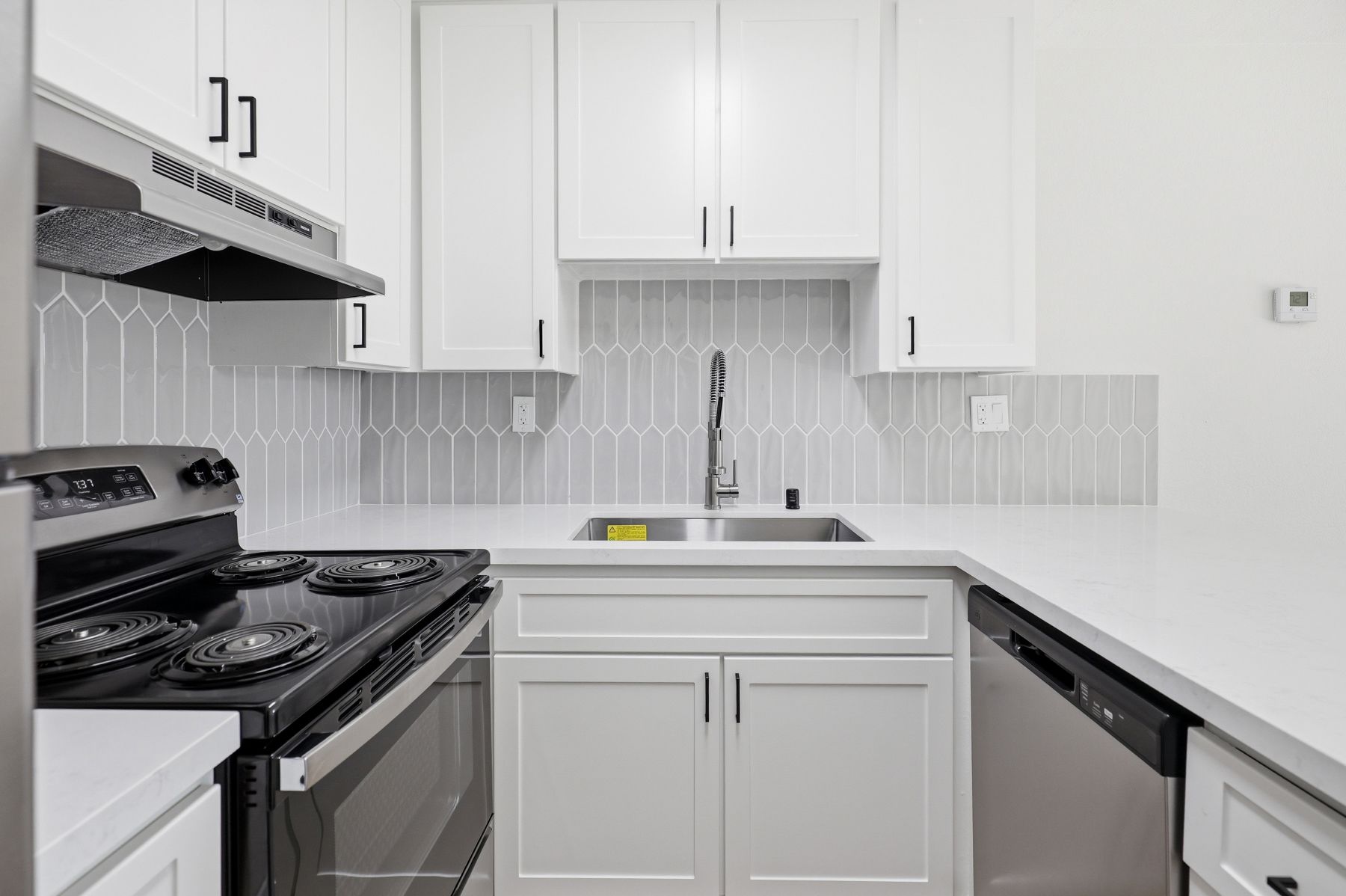 White modern kitchen with stainless steel stove, white cabinets, and gray tile backsplash