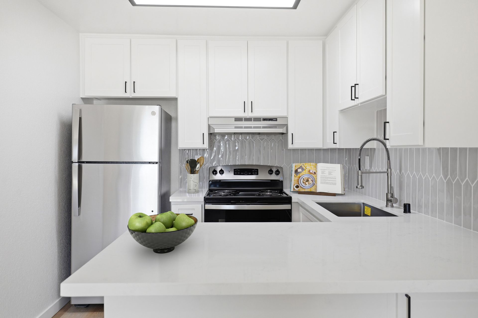 Bright white kitchen with stainless fridge, stove, white cabinets, and a bowl of green apples on the counter