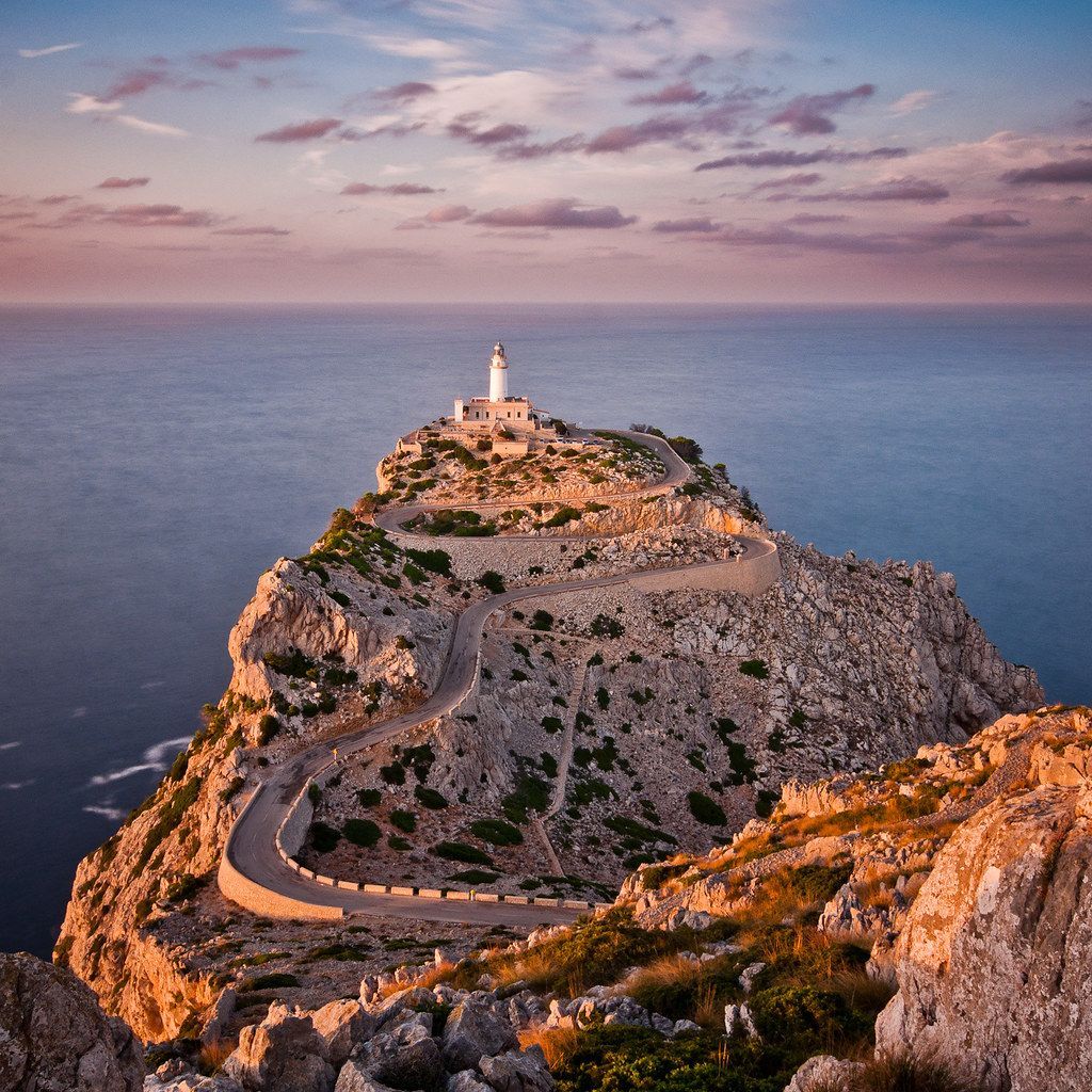 A lighthouse on top of a rocky cliff overlooking the ocean at sunset.