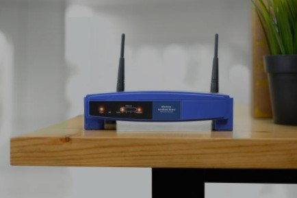 Un enrutador inalámbrico azul con dos antenas se encuentra sobre una mesa de madera.
