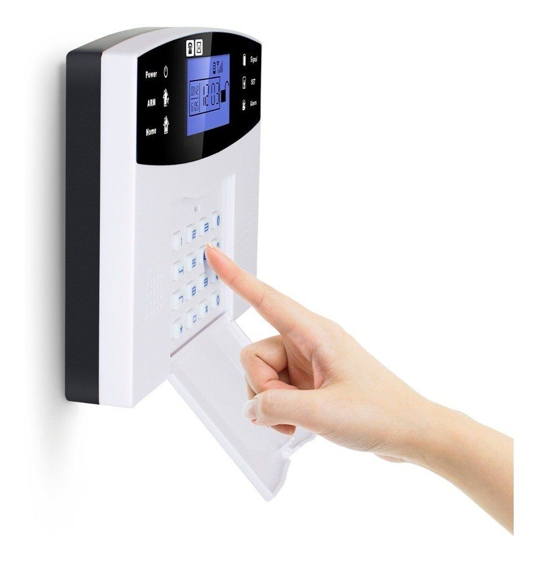 Mano ingresando código en un teclado de sistema de seguridad blanco con pantalla azul, montado en una pared.