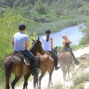 Tres personas cabalgando por un sendero cerca de un cuerpo de agua.