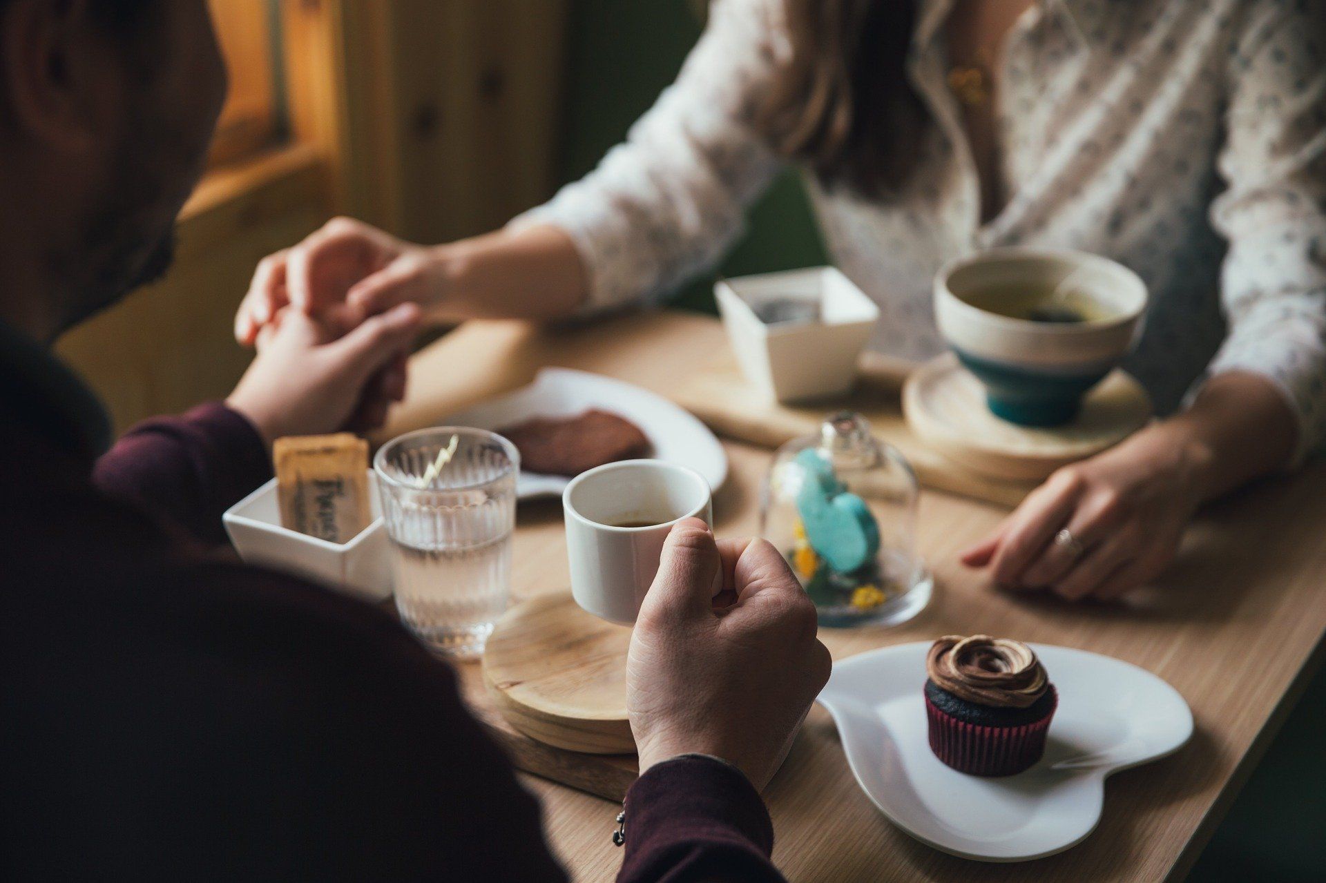 Pareja tomada de la mano en una mesa con café, dulces y una taza de té.