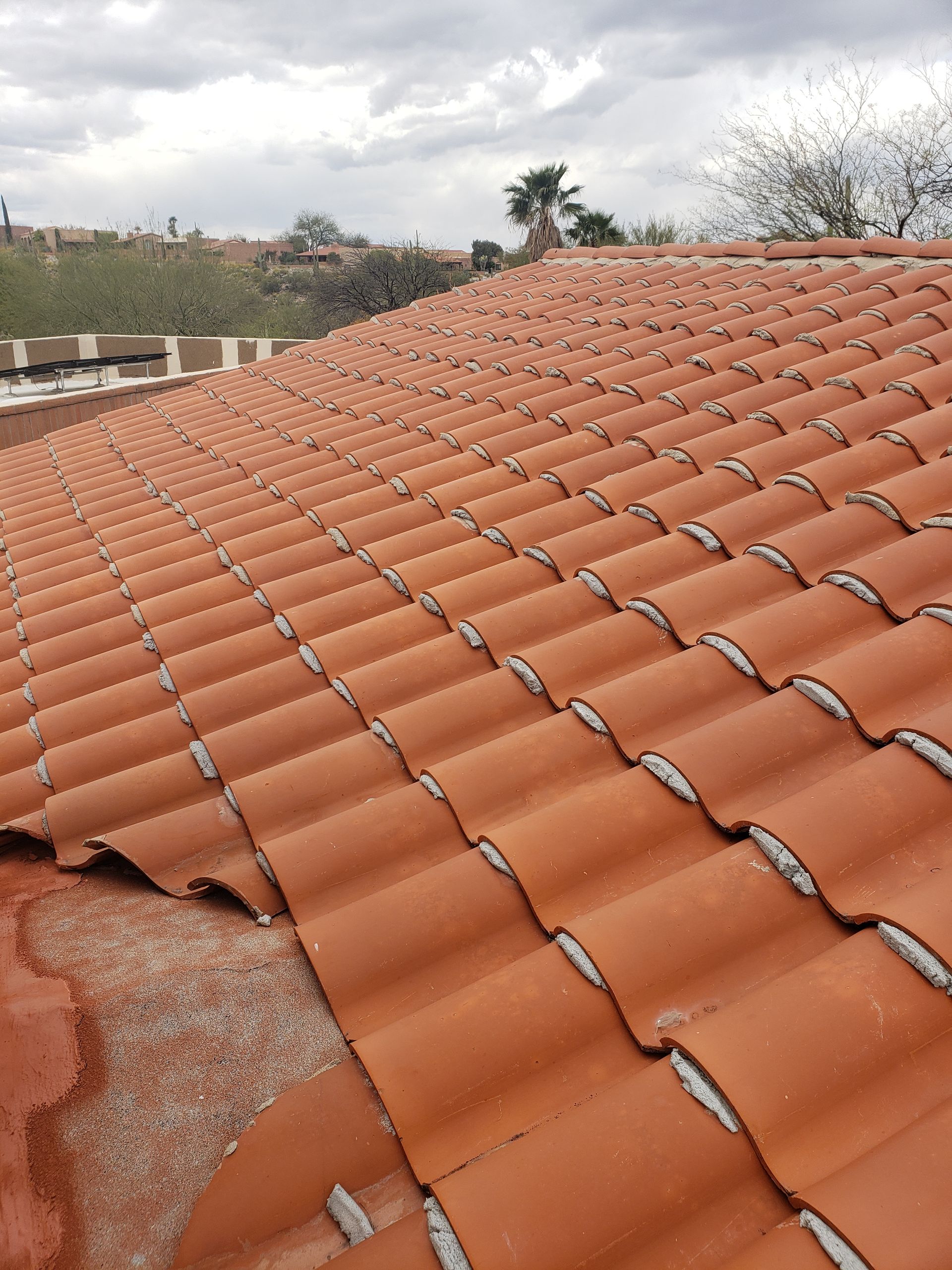 Terracotta roof tiles with a damaged section near the edge, under an overcast sky.