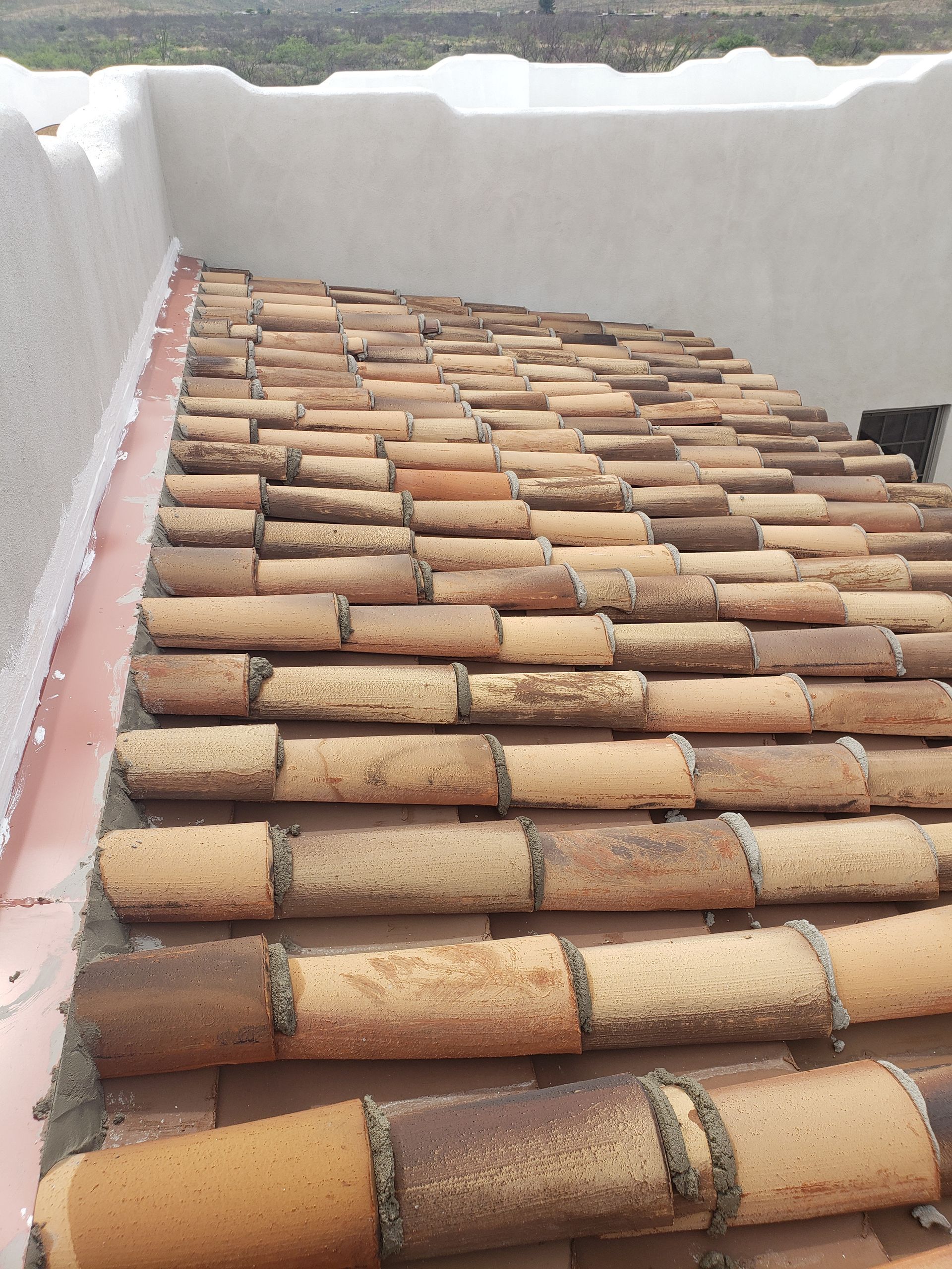 Terracotta tiled roof viewed from a rooftop between white parapet walls