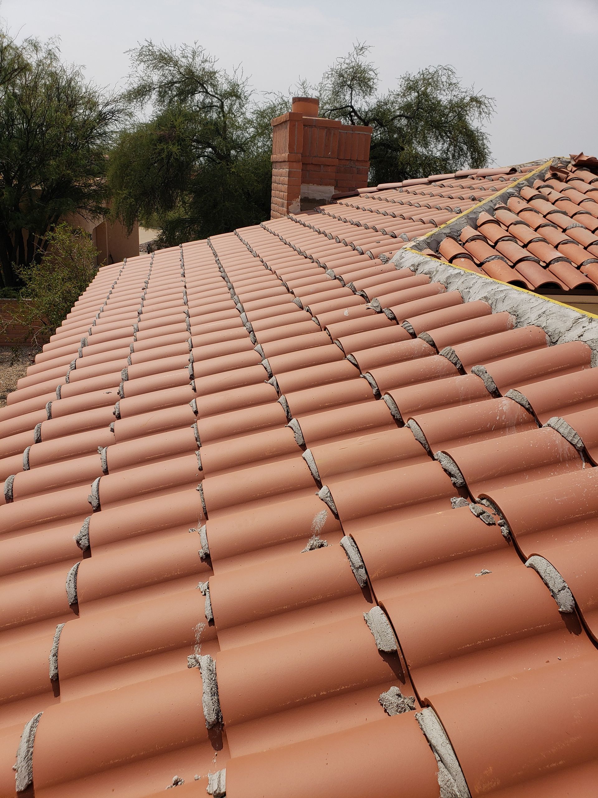 Terracotta tiled roof with a brick chimney and trees in the background