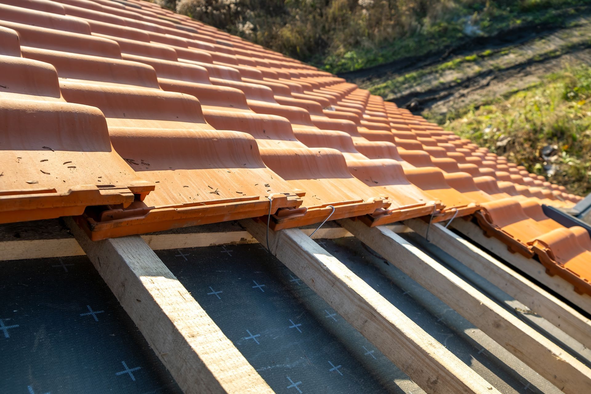 Close-up of terracotta roof tiles being installed on a roof frame with exposed wooden beams